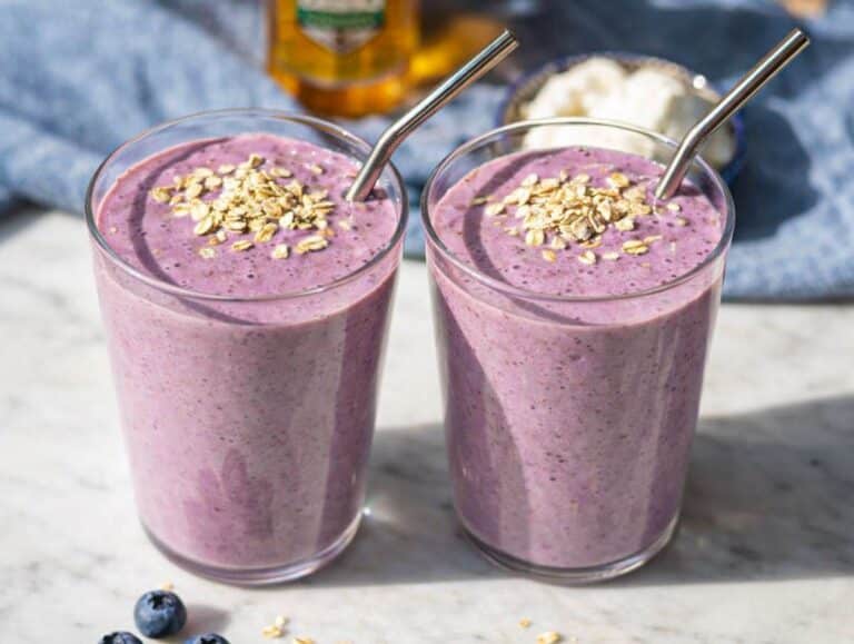 Two glasses of creamy purple Greek yogurt breakfast smoothie topped with oats on marble table in natural light.