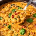 Vibrant butter beans in a creamy red sauce garnished with fresh basil in cast iron skillet.