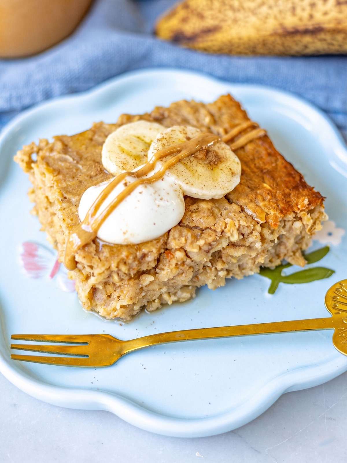 Baked oatmeal square on plate with yogurt banana slices and peanut butter drizzle.