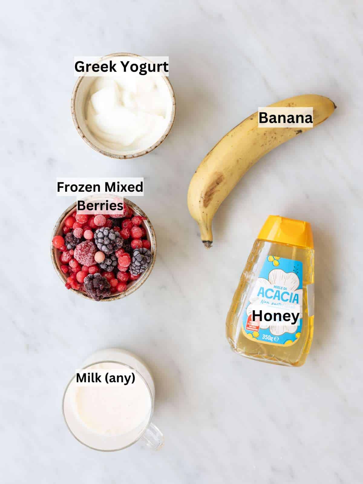 Banana, Greek yogurt, milk, and frozen mixed berries on marble table in natural light.