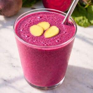 Beet smoothie in clear glass near window light with fresh ingredients in background.