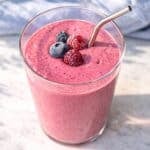 Berry smoothie in glass near window with bright natural light and soft shadows.
