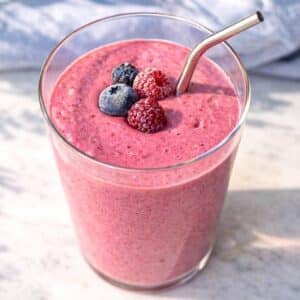 Berry smoothie in glass near window with bright natural light and soft shadows.