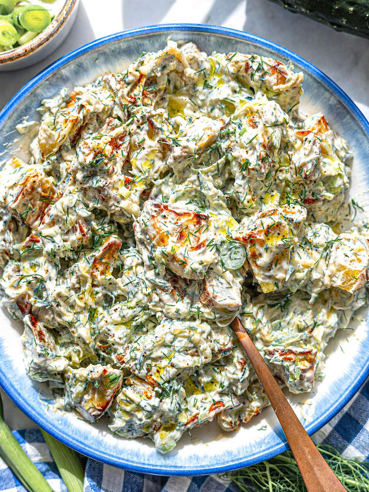 Bowl of roasted potato salad with creamy yogurt dressing and fresh herbs.