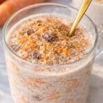 Bright mug of carrot cake overnight oats by window, topped with nuts and cinnamon.