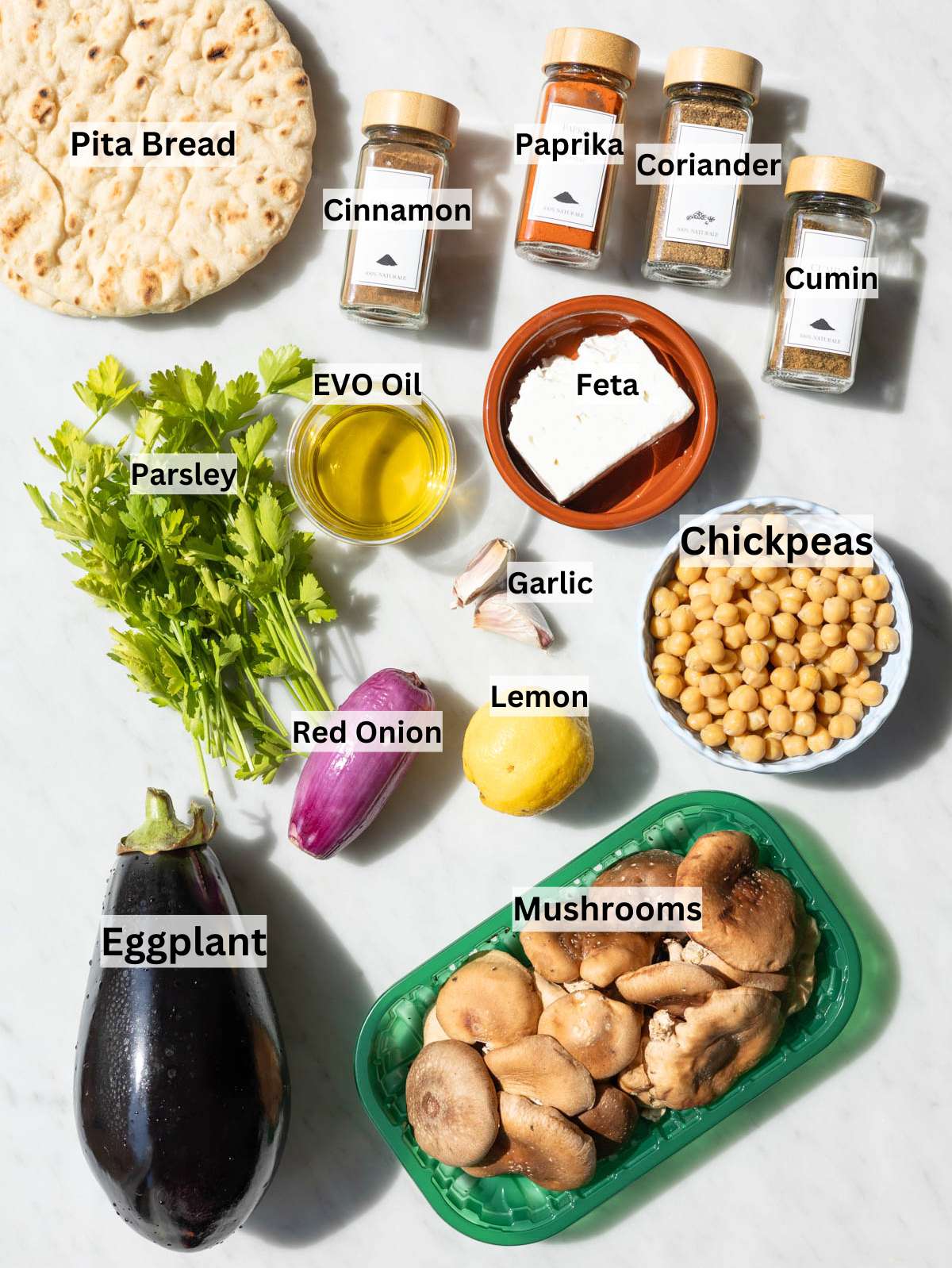 Chickpeas, eggplant, mushrooms, onion, parsley, feta, lemon on marble in natural light.