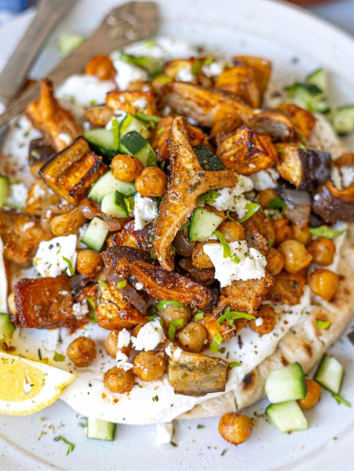 Close up of roasted vegetables and chickpeas on top of soft pita with creamy yogurt.