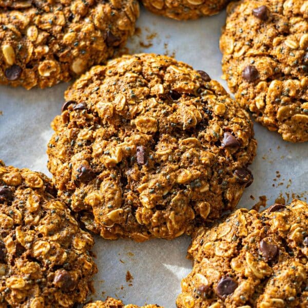 Close up of soft oatmeal cookies with seeds and chocolate chips baked on parchment.