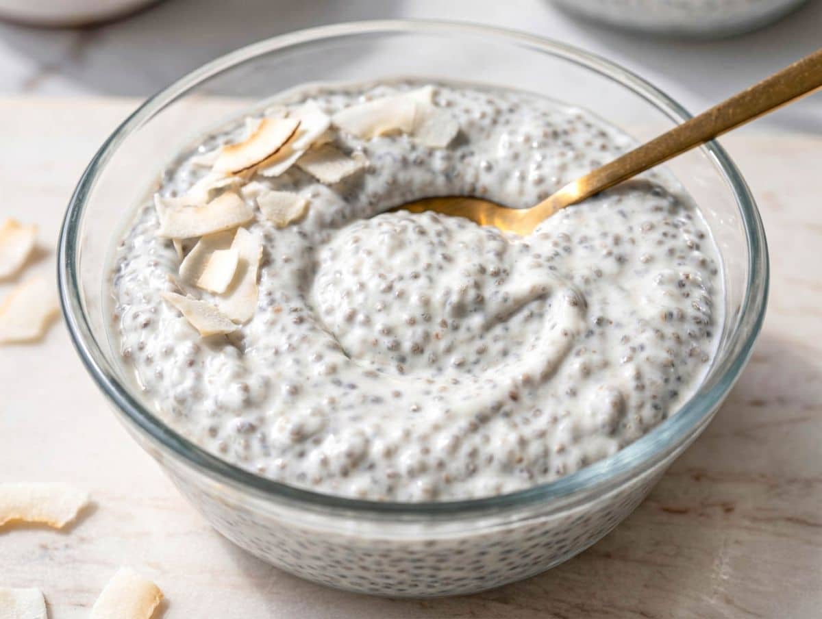 Coconut chia pudding in glass bowl with creamy texture and coconut flakes on marble table.