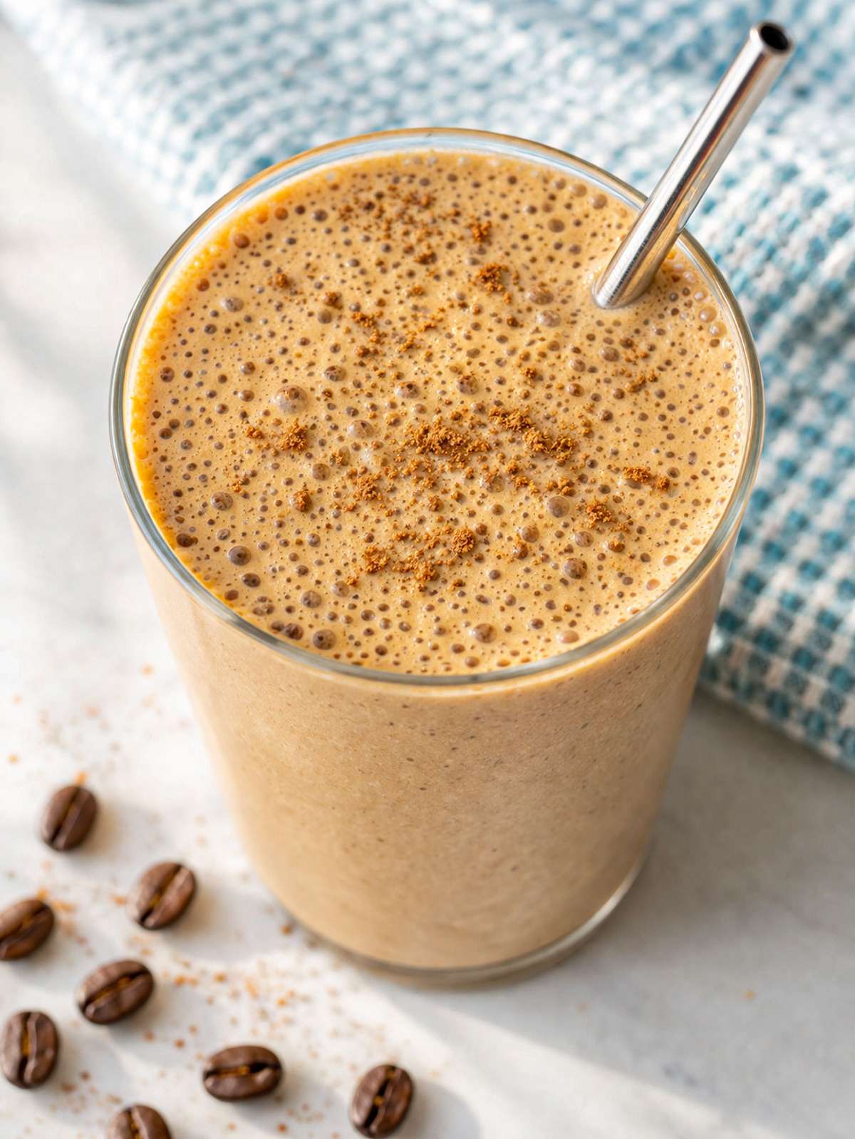 Coffee smoothie in glass on marble table with soft window light and creamy texture.
