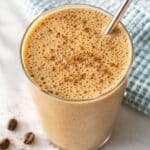 Coffee smoothie in tall glass with banana and soft natural light by window.