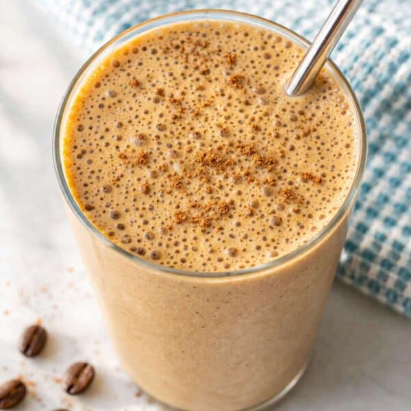 Coffee smoothie in tall glass with banana and soft natural light by window.