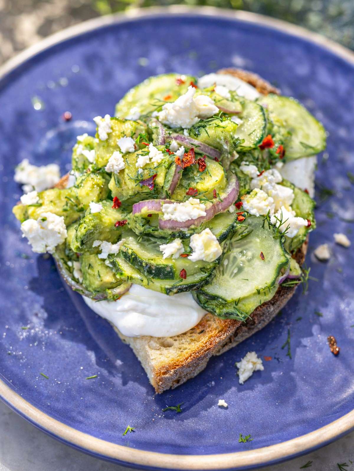 Cucumber avocado salad on toasted bread with yogurt feta and dill in natural light.