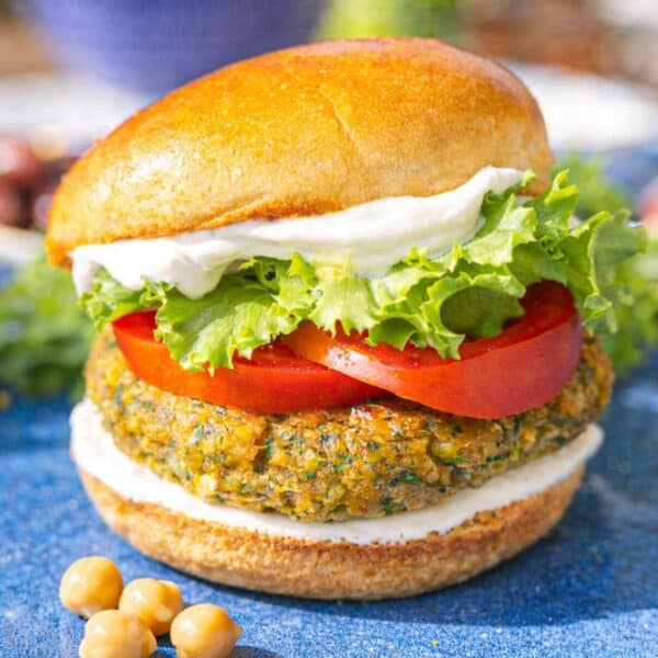 Falafel burger stacked with lettuce, tomato, and sauce, styled on marble in bright light.