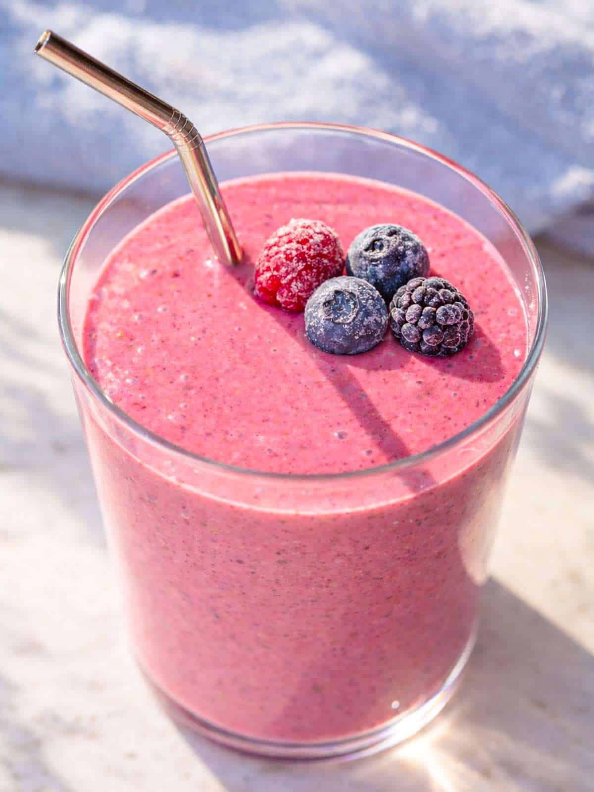 Glass of berry smoothie on marble table with soft daylight and smooth creamy texture.