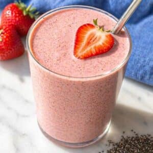 Glass of strawberry banana chia seed smoothie on marble surface.