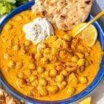 Greek yogurt chickpea curry served in bowl with naan and lemon wedge.