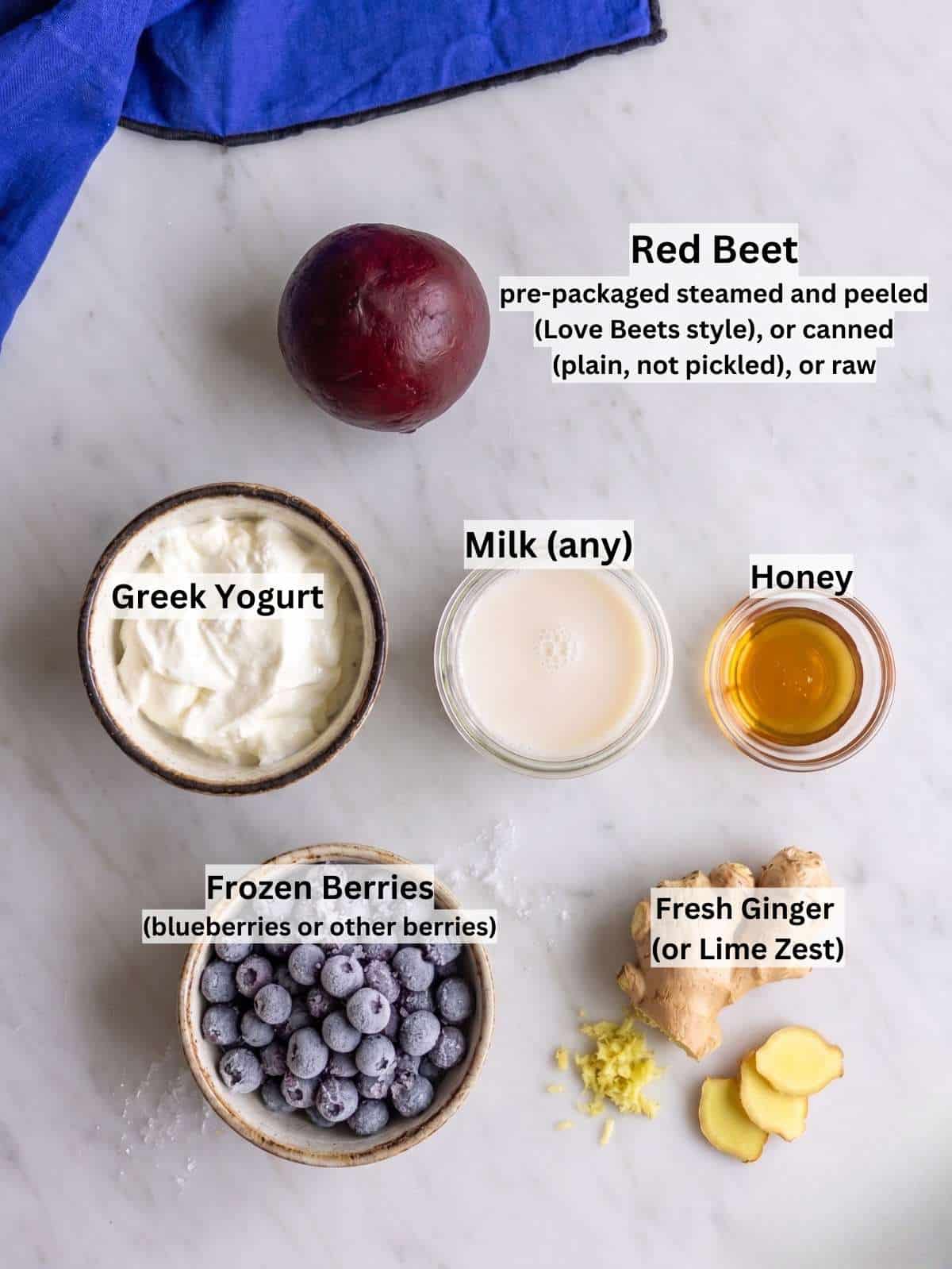 Ingredients arranged on marble table with beet, berries, yogurt, honey, almond milk, ginger.
