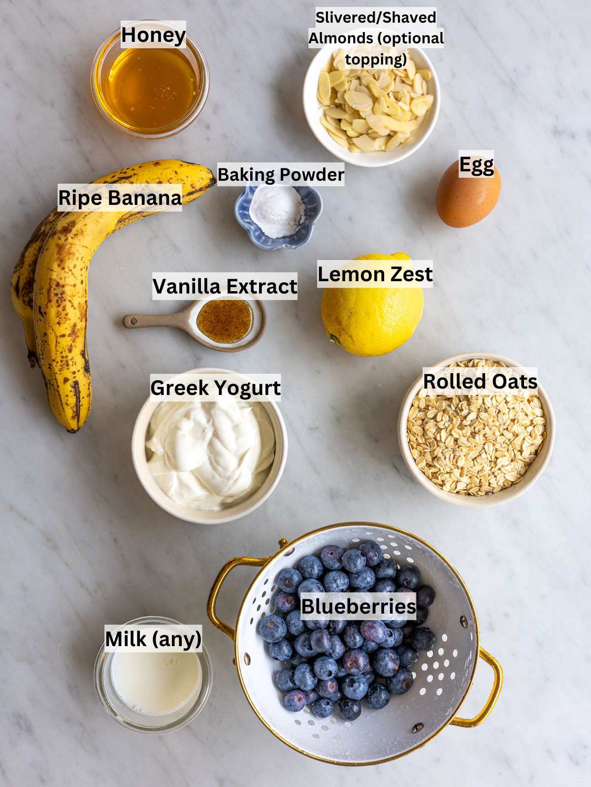 Ingredients for blueberry baked oatmeal cups on marble surface in soft natural window light.