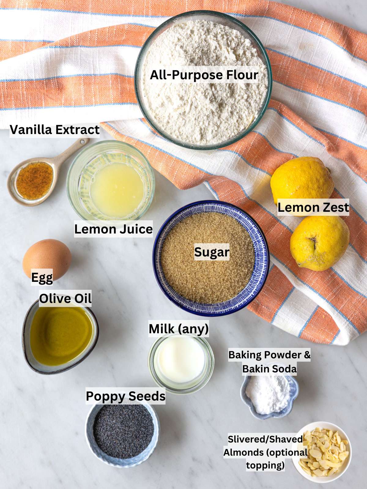 Ingredients for lemon poppy seed muffins arranged on marble surface near bright window.