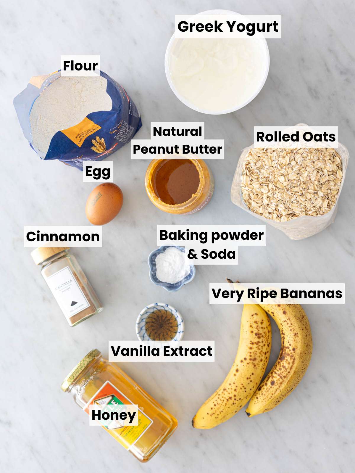 Ingredients for peanut butter banana muffins arranged on marble surface in natural window light.