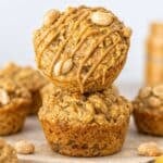 Peanut butter banana muffins stacked on marble surface with creamy drizzle and oats in soft natural light.