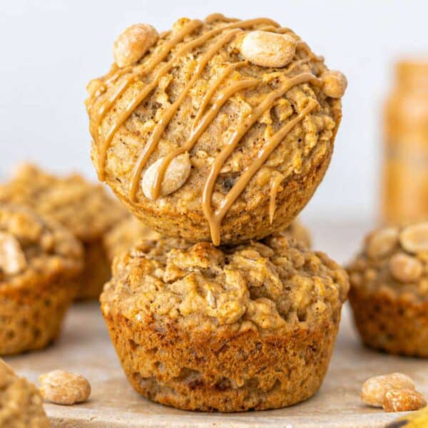 Peanut butter banana muffins stacked on marble surface with creamy drizzle and oats in soft natural light.