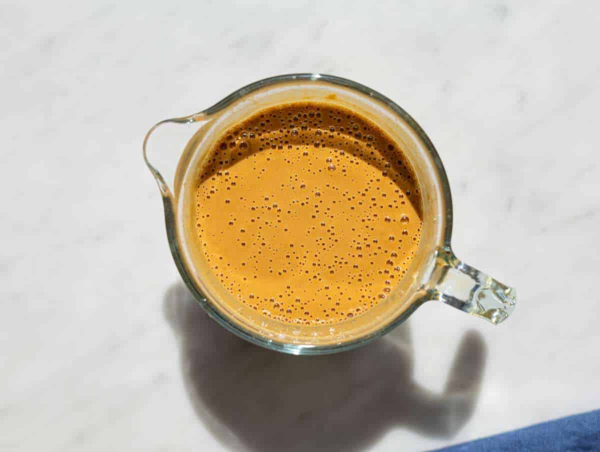Peanut dressing blended until smooth and creamy in a glass jug on marble surface.