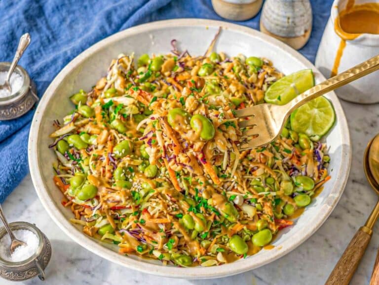 Peanut dressing poured over cabbage salad, coating vegetables evenly.