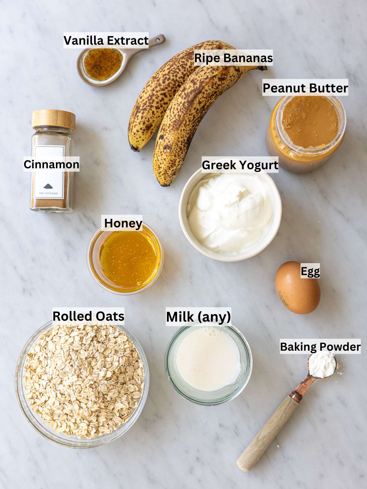 Ripe bananas oats Greek yogurt peanut butter and honey on marble surface in natural light.