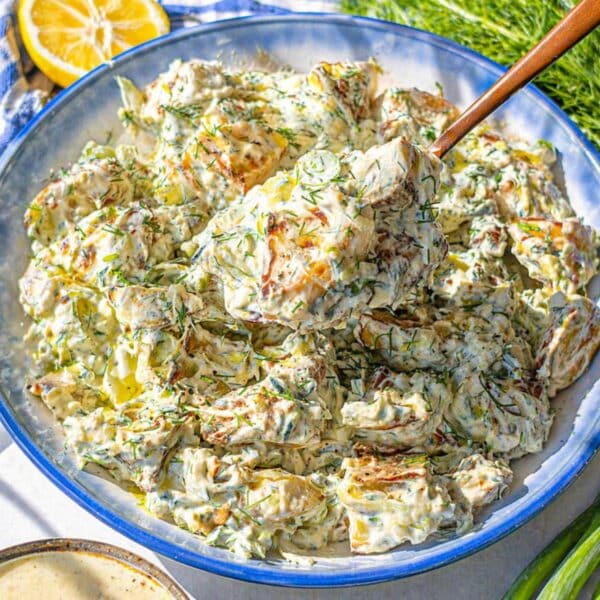 Roasted potato salad served in a bowl on marble table with soft natural light.
