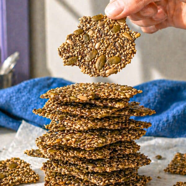 Seed crackers stacked loosely on a plate with soft natural light on marble.