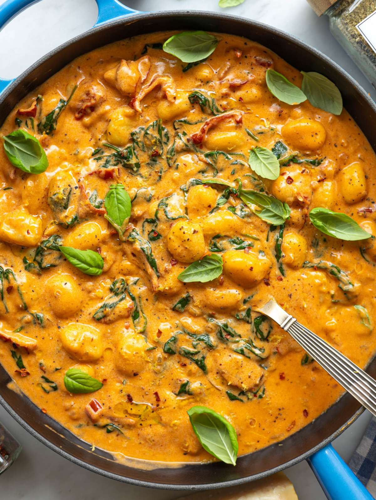 Skillet of creamy gnocchi with basil leaves on marble table near bright window light.