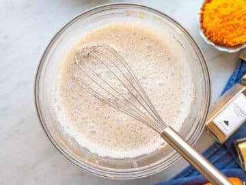 Step 1 Greek yogurt, milk, and spices being whisked in bowl on marble surface.