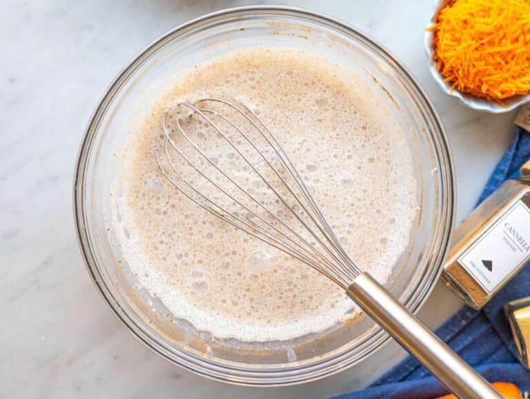 Step 1 Greek yogurt, milk, and spices being whisked in bowl on marble surface.