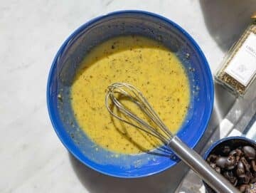 Step 1 Whisking olive oil dressing in bowl with herbs and mustard on marble table.