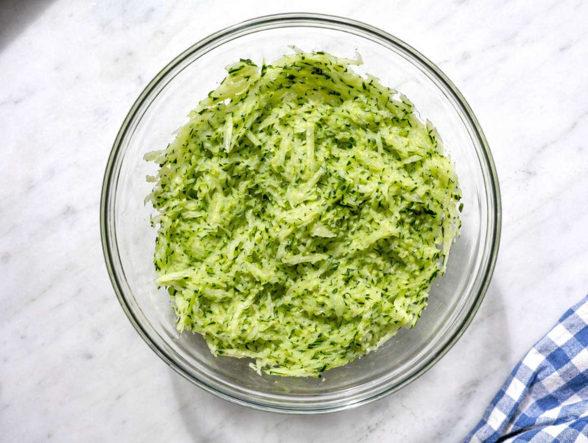 Step 2 Grated cucumber being squeezed by hand to remove excess moisture.