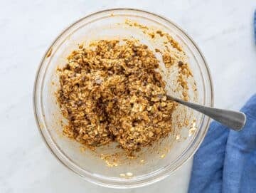 Step 2 Thick cookie dough with oats, seeds, and chocolate chips being mixed with a spoon.