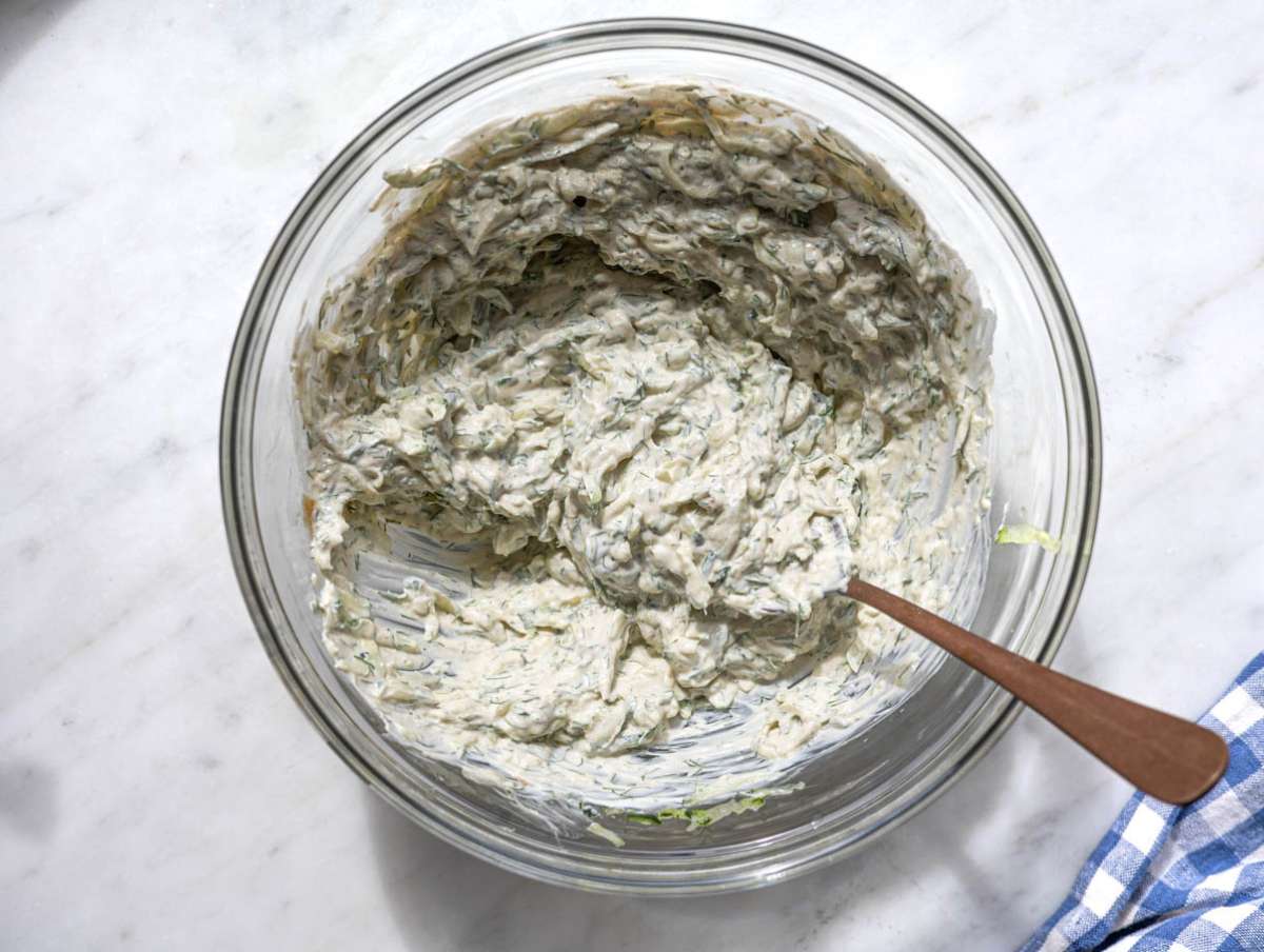 Step 3 Mixing bowl with yogurt, tahini, cucumber, and herbs being stirred.
