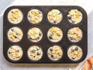 Step 3 Oat batter spooned into muffin pan cups on marble surface in bright light.