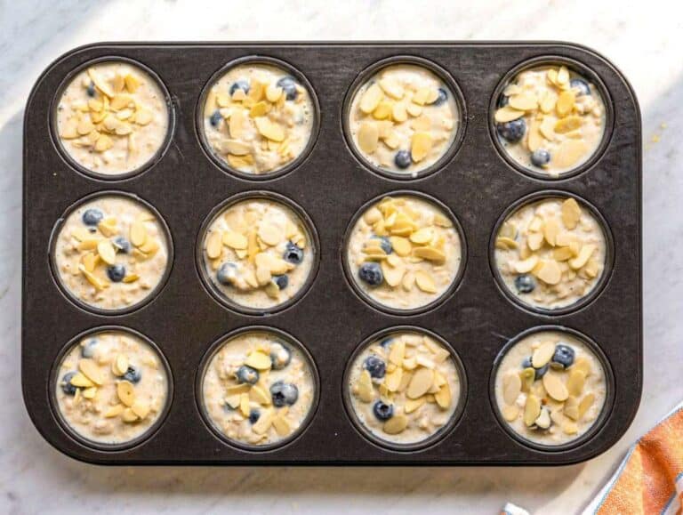 Step 3 Oat batter spooned into muffin pan cups on marble surface in bright light.