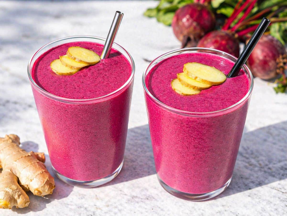 Two glasses of beet smoothie on marble table with sliced fresh ginger.