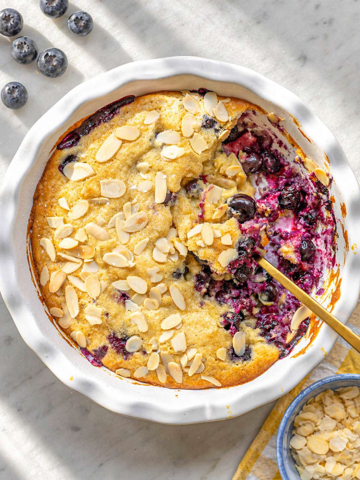 Warm blueberry spoon cake in a pie dish with golden top and juicy berries.
