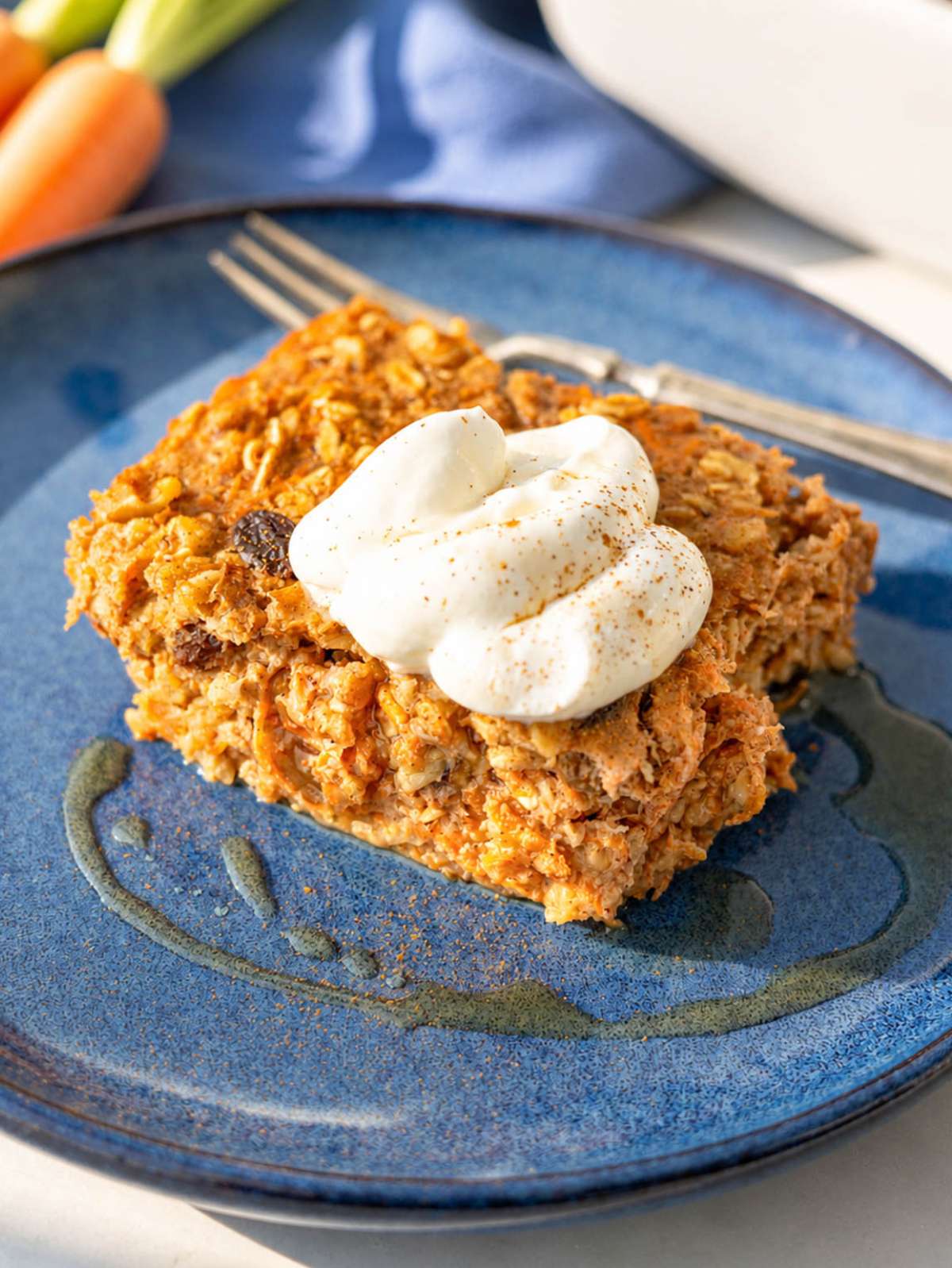 Carrot cake baked oatmeal served on blue plate with yogurt topping and light drizzle.