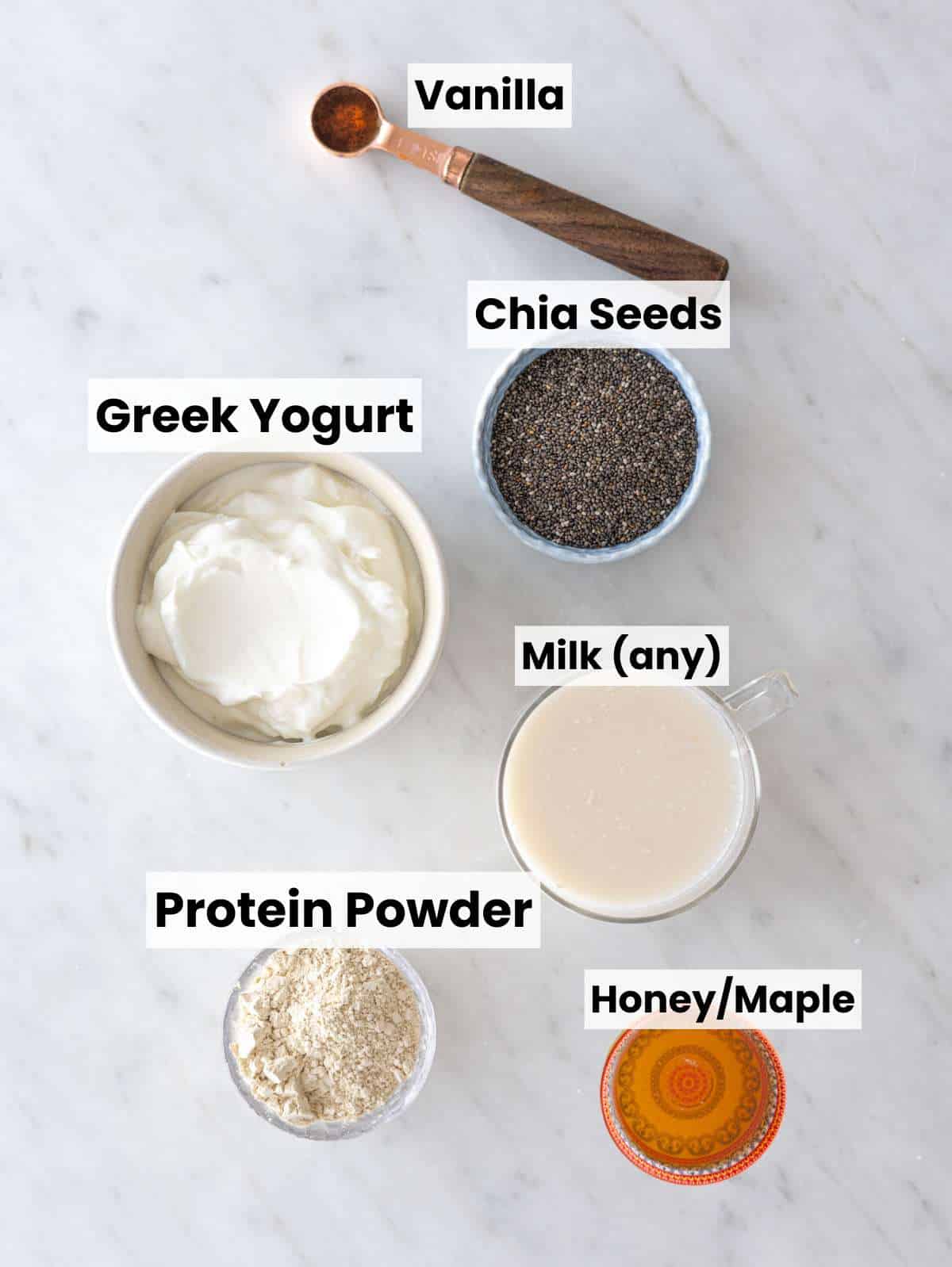 Chia seeds, Greek yogurt, milk, protein powder, and maple syrup on marble surface.