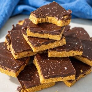 Chocolate peanut butter bars stacked on marble surface with crisp chocolate topping and natural light.