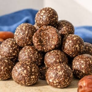 Close-up of chewy chocolate date energy balls stacked on marble surface near natural window light.