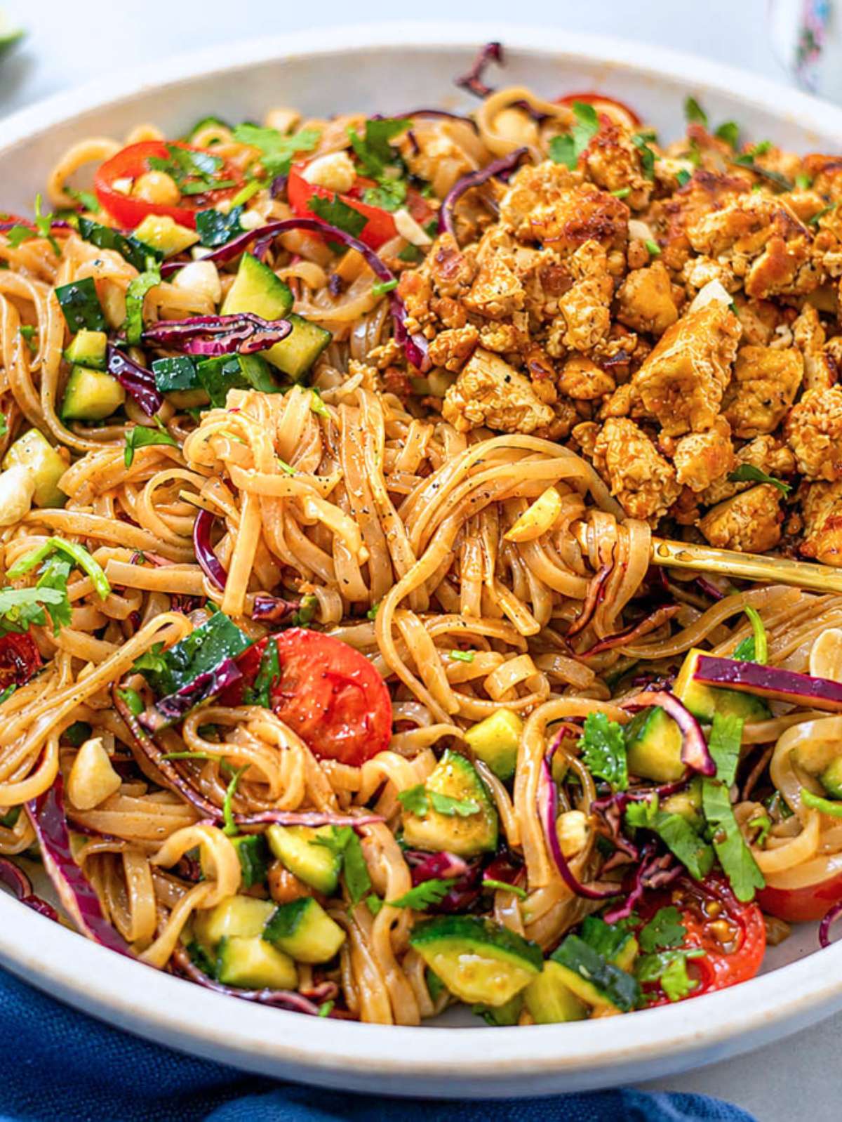 Close-up of crumbled tofu over noodles, cabbage, and cherry tomatoes.