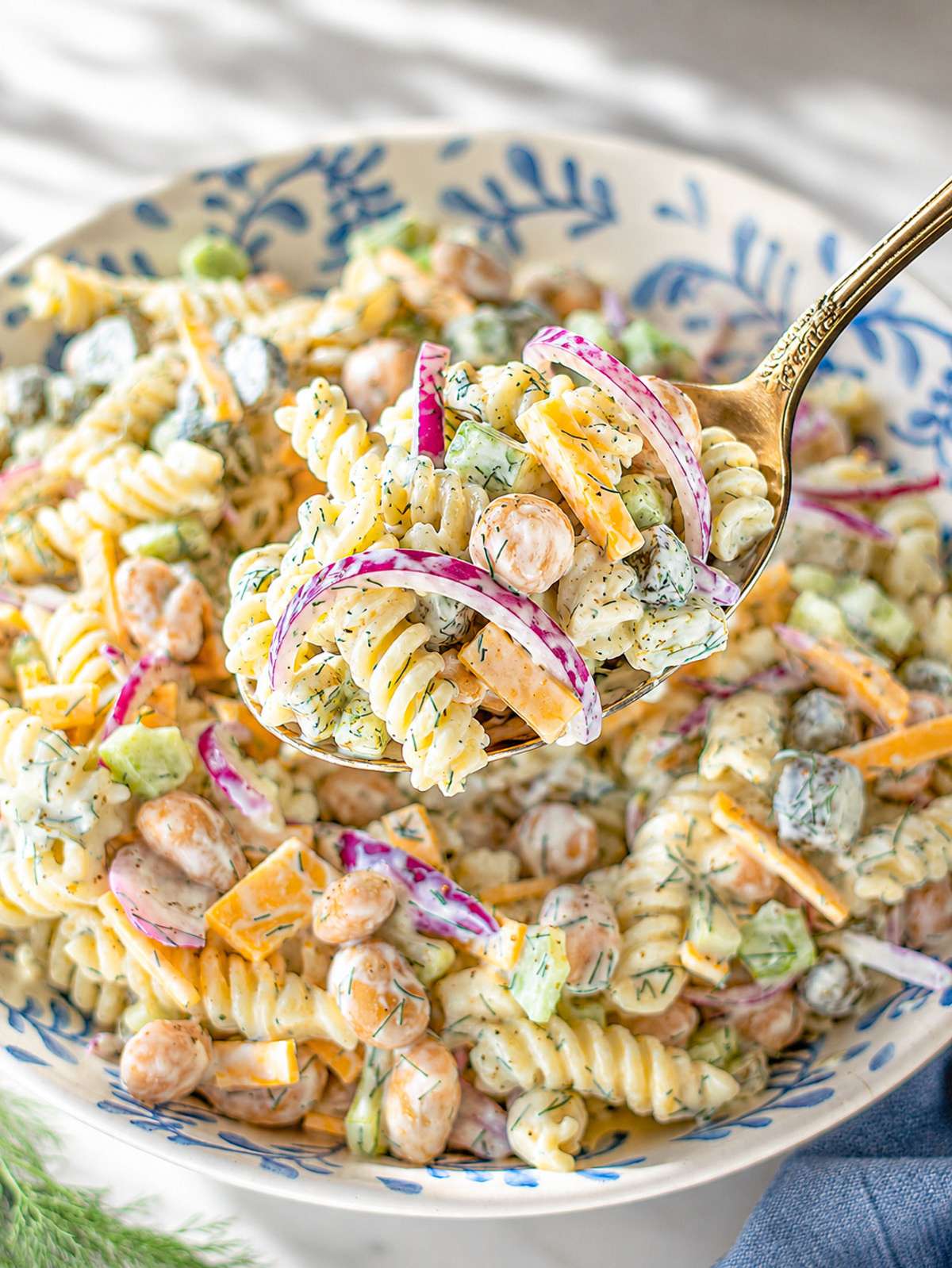 Close-up of pasta salad coated in creamy Greek yogurt dill dressing with celery and pickles.