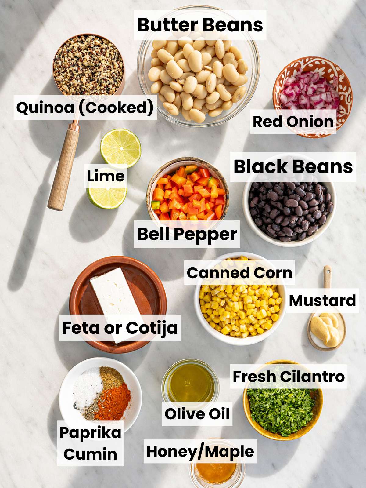 Colorful Mexican bean salad bowl ingredients arranged on white marble countertop in natural window light.